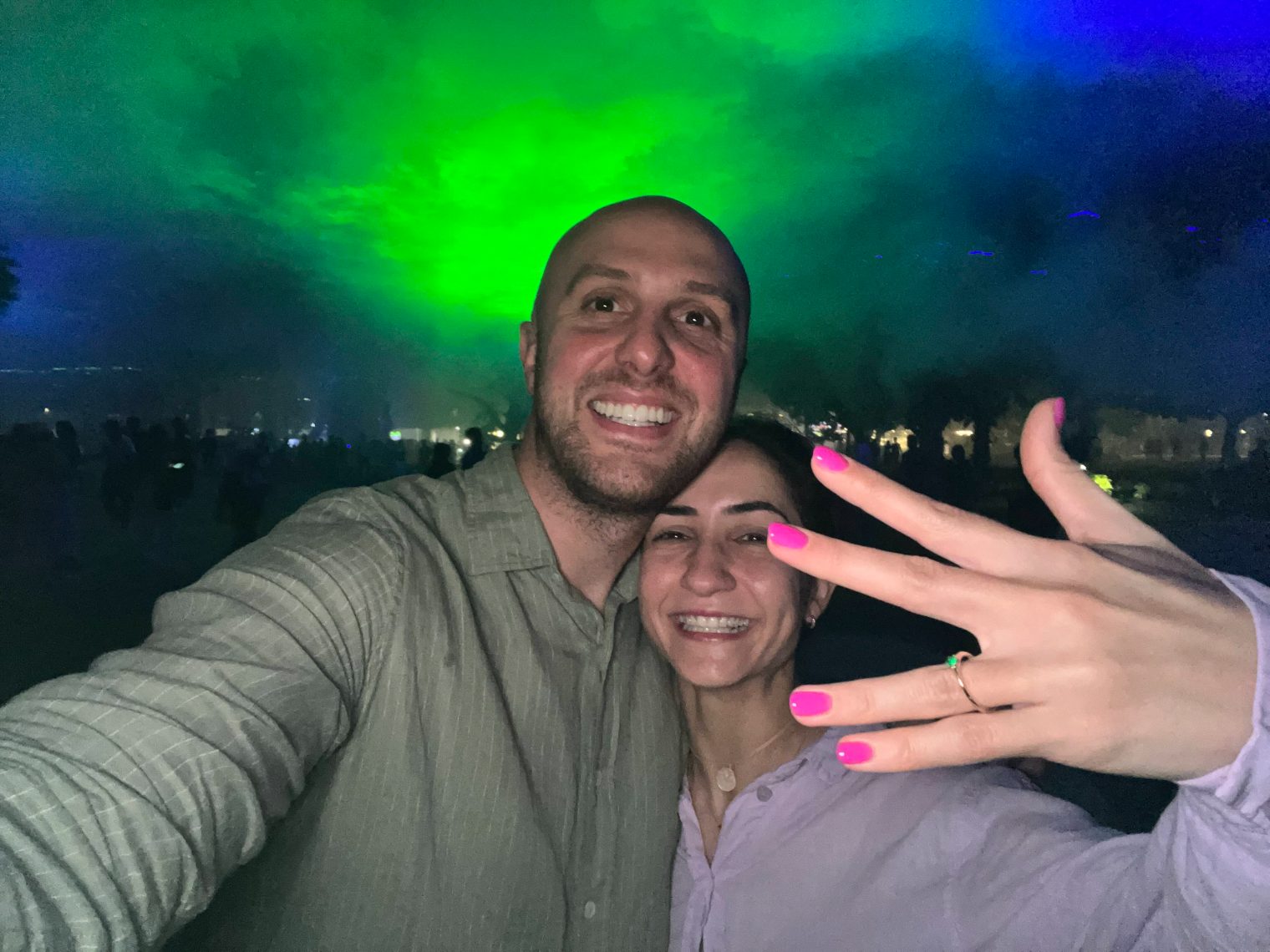 Elena and Todor smiling cheek to cheek at night, Elena holding up her hand to show the engagement ring.