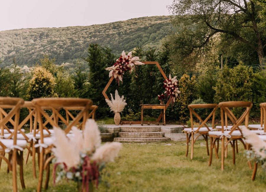 The hexagonal floral ceremony arch and cross-back chairs at Pasarel Lake Club, framed by forested hills.